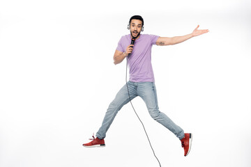 Fototapeta na wymiar positive man in wireless headphones singing in microphone and levitating on white.