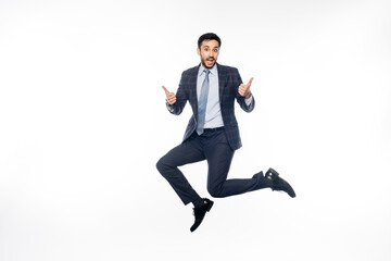 amazed businessman in suit jumping while showing thumbs up on white.