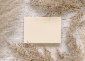 Blank card on white wooden table near dried pampas grass