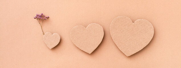Family concept. Three cardboard hearts - parents and a child with a flower on a beige background. Top view. Web banner