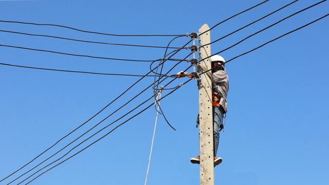 Technician connecting wires on electric poles. Employees hung with belts on electric poles to install low voltage cables on concrete poles on a blue sky background with copy space. selective focus