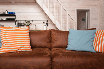 Old brown leather couch in wooden house background. Aged orange sofa skin with pillows , interior in natural day light