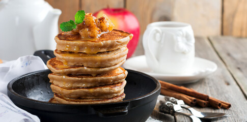 Stack of pancakes from buckwheat flour with baked apples and cinnamon on old wooden background. A...