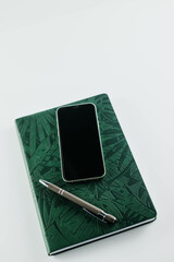 Flat lay of, cell phone, pen, and green notebook on white background
