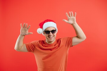 Portrait of happy and excited man in santa hat, rejoicing and winning something, celebrating new year, standing over red background