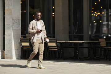 Full length portrait of adult African-American man walking in urban city street, copy space