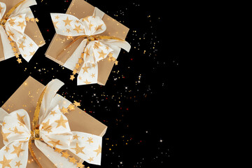 Golden gift boxes decorated with stylish bow falling and flying against a black background with...