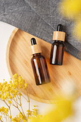 Amber glass dropper bottles with bamboo lid on wooden plate for product presentation. Top view background with dry plants. Skincare cosmetic with yellow dry plants and fabric. Beauty concept for face