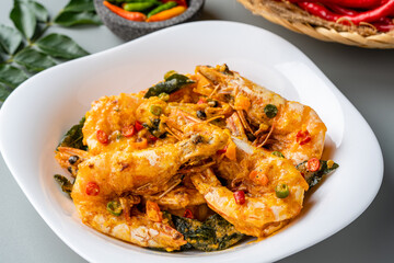 udang saus telur asin or Salted egg fried shrimp with curry leaves served on white plate and isolated on gray background.