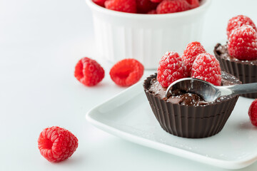 Chocolate raspberry mousse cups with a spoon on a small platter.
