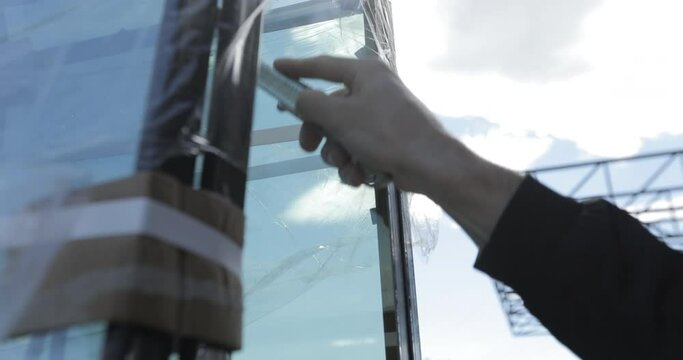 hand cuts the tape with a knife from a glass window unit before unloading at a construction site against the backdrop of a clear sunny sky. Close-up