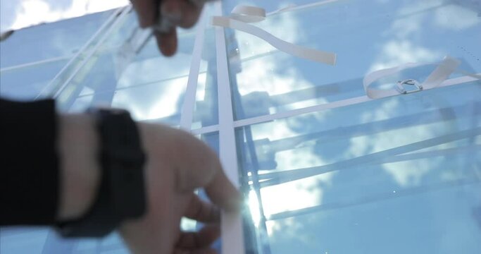 Bare hands with a clock cut the white tape on a large metal-plastic window that is ready to be unloaded against the backdrop of a clear sunny sky. large glass unit before installation. close-up