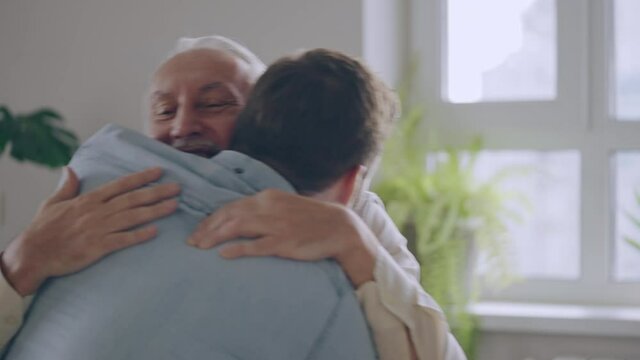 Happy senior father and adult son hugging on couch, family love and support