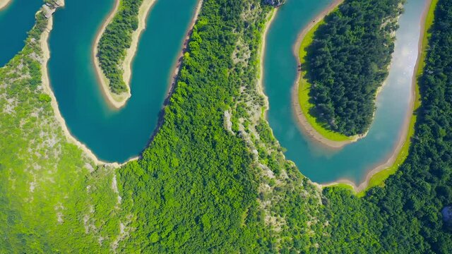 Aerial view of green grass forest with tall pine trees and blue bendy river flowing through the forest in Finland
