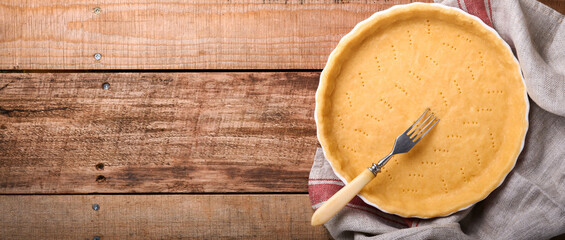 Dough for baking quiche, tart or pie in ceramic baking form ready for bake on kitchen towel over old rustic plank wooden background. Top view, copy space. Concept homemade baking for holiday.