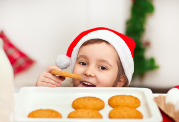 Kid girl in Santa cap taking try to steal cookie from table.