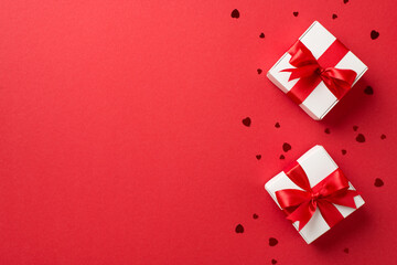 Top view photo of valentine's day decorations white gift boxes with red ribbon bows and heart shaped confetti on isolated red background with blank space