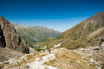 Group of trekkers backpackers descending from Ak-Sai Racek Hut and Glacier to Ala-Archa. Ala Archa Alpine National Park Landscape near Bishkek, Tian Shan Mountain Range, Kyrgyzstan, Central Asia.