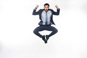 businessman in suit jumping while showing muscles on white.