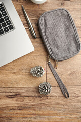 Make-up bag and pine cones next to laptop on wooden table, view from above