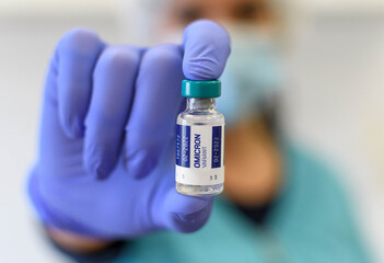 Close-up photo of medical worker holding covid vaccine vial with omicron variant text on label