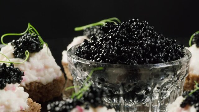 Black caviar sandwiches close-up. Beluga sturgeon salted roe in glass bowl. Raw seafood. Luxury delicacy food. Delicious and tasty fish products. Russian cuisine. Festive dinner.