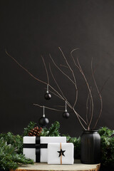 Vase with tree branches decorated with black baubles and Christmas presents wrapped in white paper