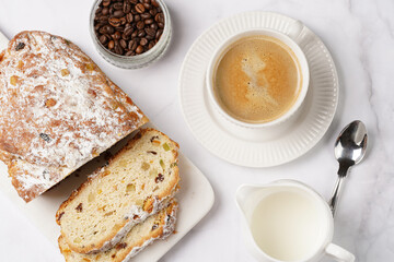 White porcelain cup with coffee cappuccino on a white saucer plate and christmas pastry stollen on a marble table