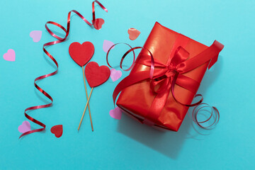 Red box with red ribbon on a blue paper background. Valentine's Day gift with confetti and decor