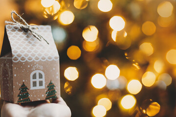 Merry Christmas and Happy Holidays! Hand holding christmas gift box ih house shape on background of...