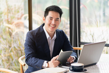 Asain businessman working on digital tablet while sitting beside window in cafe, asian man working...