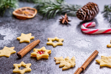 Christmas sweets and cookies in form of christmas tree placed on gray desk with pine cone and branch on the side. Winter and christmas decorations, cinnamon, sugar and star anise.