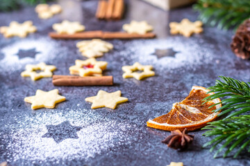Christmas sweets and cookies placed on gray desk. Winter decorations, pine tree and cone. Concept of christmas, gifts and holidays. Glowing lights in the background.
