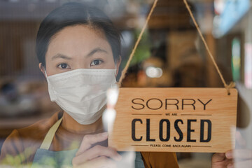 Asian young owner retail,coffee shop woman turning sign board to closed with wearing face...