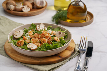Arugula salad with shrimp and champignons, olive oil and dill on a wooden board on a white surface
