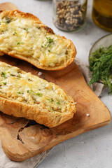 Two halves of garlic and butter bread - baguette on a wooden board, sea salt, pepper, dill and garlic cloves on a grey concrete background, top view