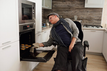 Contemporary man with disability taking homemade cookies out of electric oven in kitchen environment