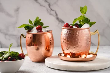 Fototapeten Traditional american alcoholic beverage moscow mule in copper mugs with cranberry and mint on white marble board - non-alcoholic cocktail version © Romana
