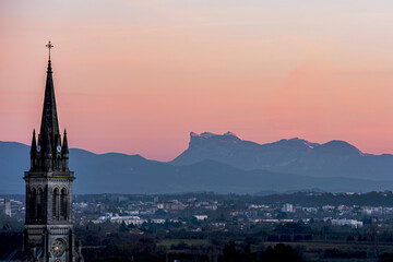 Beautiful sunset over french Vercors mountains with the snow on the top and a church tower of the Cornas village on the foreground.