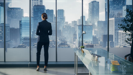 Fototapeta premium Successful Businesswoman in Stylish Suit Looking out of the Window at Big City in Downtown Area. Confident Female CEO Working on Investment Opportunity. Real Estate Agent Planning a Development Deal.
