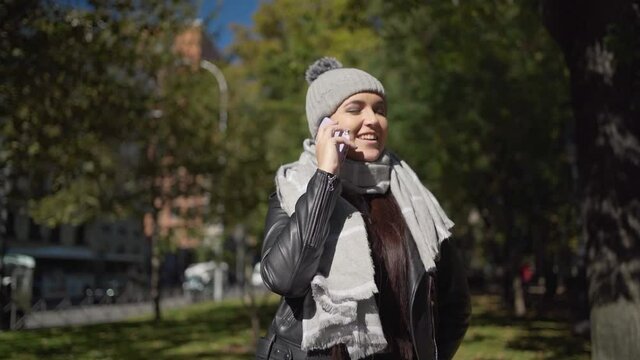 Positive young woman smiling and talking on smartphone on street
