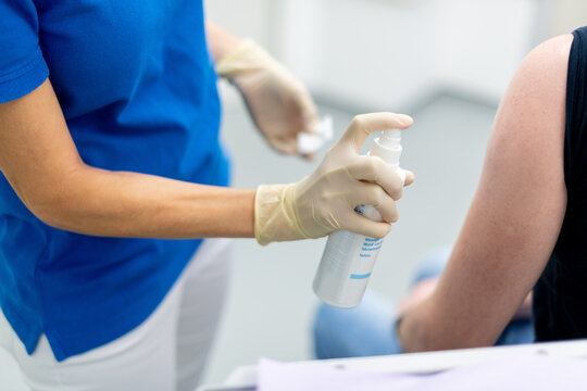 Desinfektionsspray wird auf den Oberarm gesprüht, Vorbereitung einer Impfung.