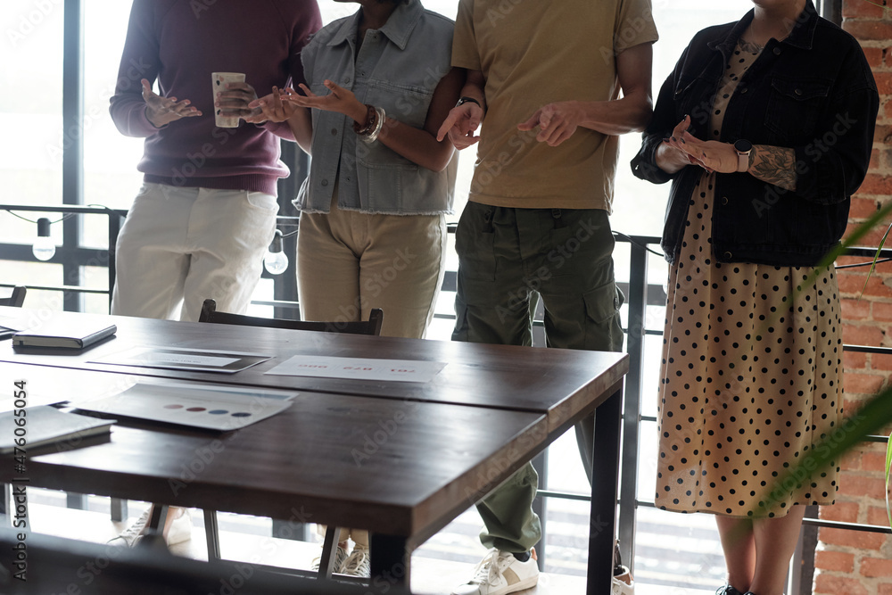 Poster Row of four young office workers standing in front of wooden table with papers and discussing working points at meeting