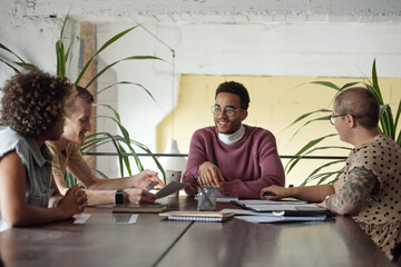 Group of young successful economists in casualwear sitting by table in office and discussing plans...