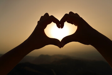 Woman hands silhouette framing sun making heart shape