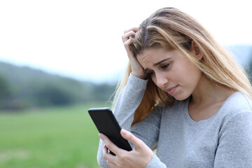 Worried teenage girl checking phone message outdoors