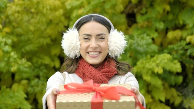 Woman presenting Christmas gift standing in front of trees