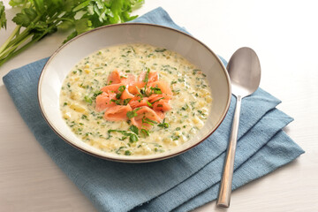 Vegetable soup of parsley and potatoes with salmon strips on a blue napkin and a white table, selected focus