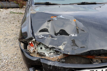 Front view close up of a crashed car. Broken headlight and dent on the hood of a black car.  Car after an accident.