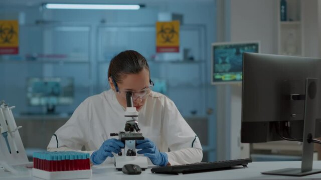 Lab worker using magnifying glass on microscope to work on science experiment. Woman chemist analyzing dna substance with microscopic lens on optical tool in laboratory. Biology researcher
